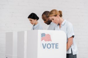 side view of women and african american man voting near vote lettering and brick wall