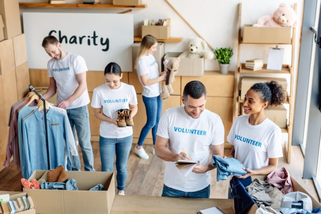 young, cheerful multicultural volunteers in white t-shirts with volunteer inscriptions working in